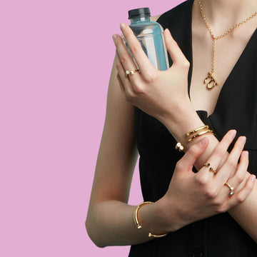 Woman holding a small plastic bottle, wearing a set of gold rings and bracelets.