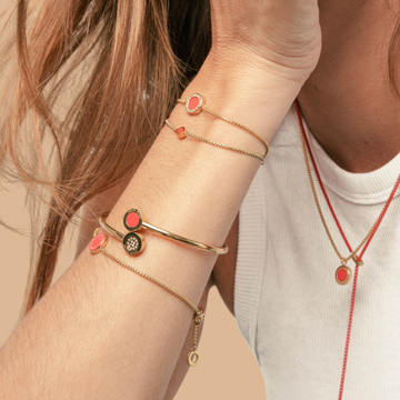 Close-up of a woman's arm wearing layered gold bangles and bracelets with red enamel details.