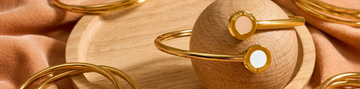 Gold bangle bracelets with white and nude recycled plastic details on a wooden sphere.