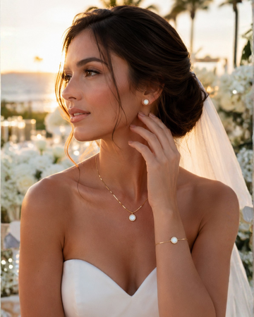 Bride wearing delicate gold necklace, bracelet, and earrings at a sunset beach wedding.