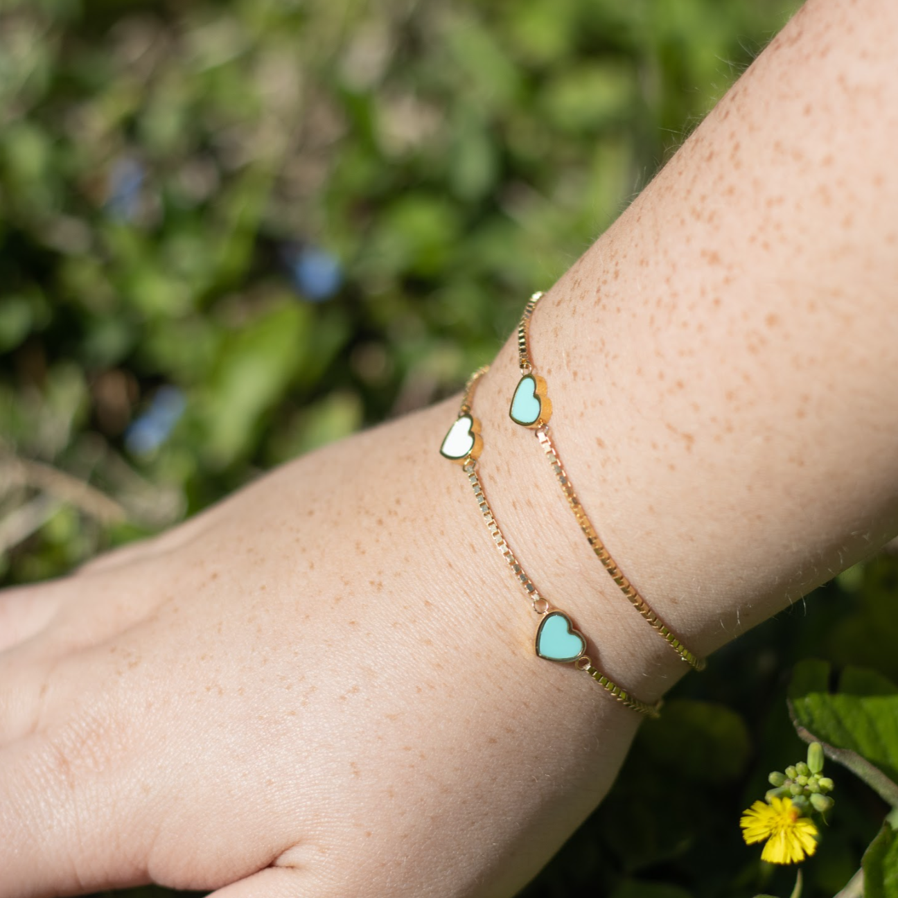 Two gold chain bracelets with alternating white and turquoise heart charms.