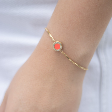 Jason Hyde gold chain bracelet with a round coral charm on a person's wrist.