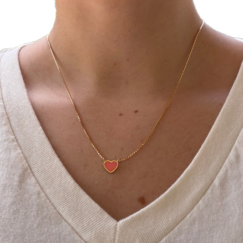 Woman wearing a Jason Hyde gold necklace with a coral heart pendant.