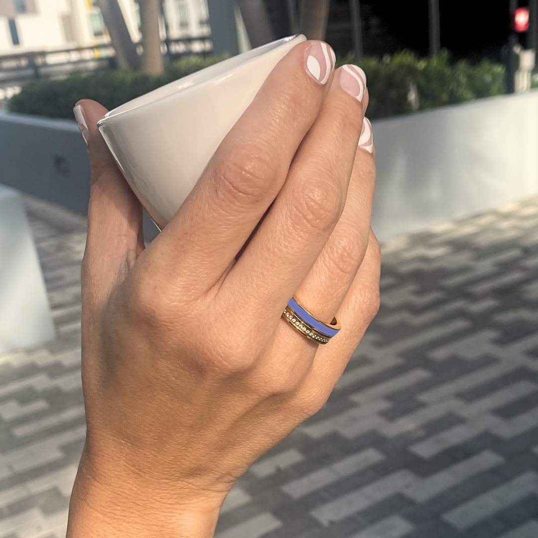 Woman’s hand holding a cup, wearing Jason Hyde gold and persian blue enamel ring 