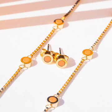 A product flat lay of a Jason Hyde gold necklace and stud earrings with orange enamel details.