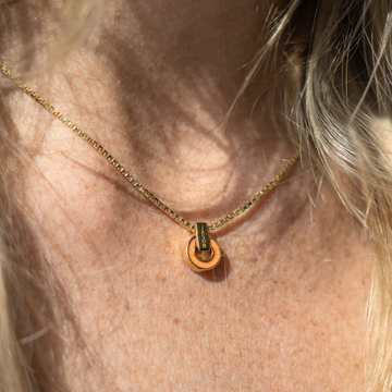 A close-up of a Jason Hyde necklace with an orange charm