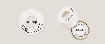 White jewelry with "seacap" and "JASON HYDE" branding, resembling a bottle cap.