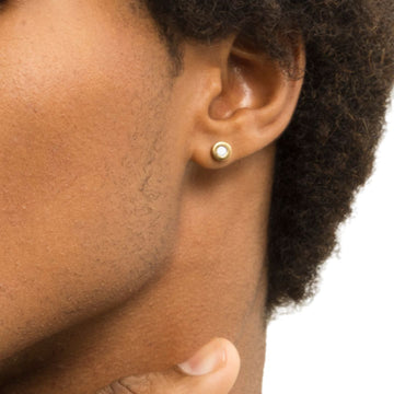 A gold stud earring with a white recycled plastic chip on a man's earlobe.