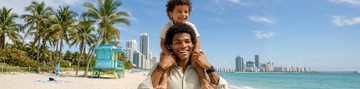 A smiling man gives his young son a shoulder ride on a sunny beach
