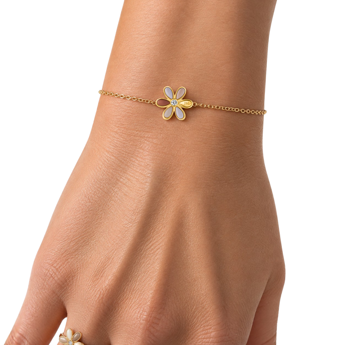 Dainty gold chain bracelet with a beige flower charm on a wrist.