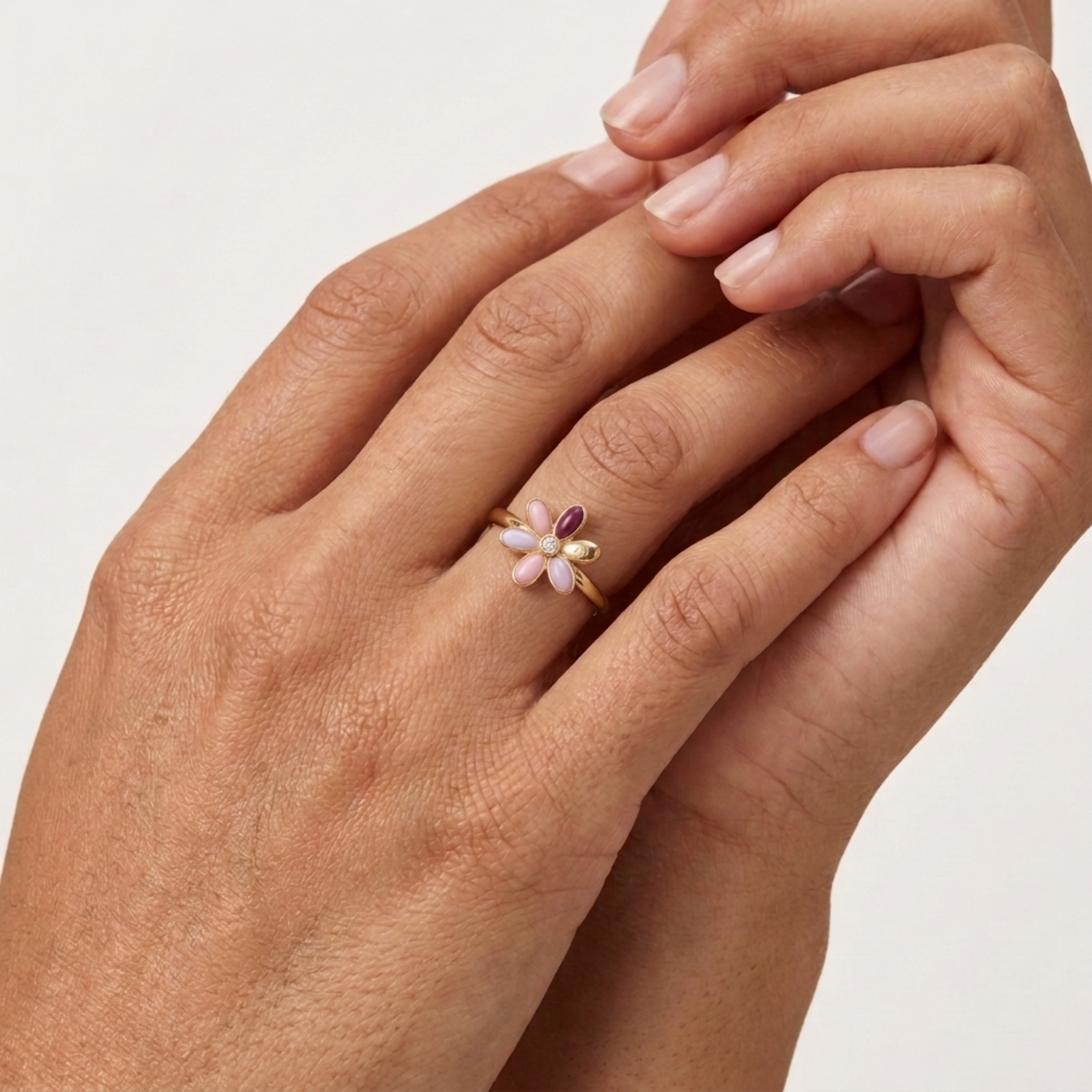Gold-tone sea-flower ring with burgundy and blush enamel petal cluster on fingers