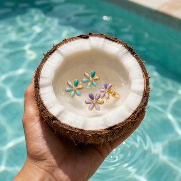 A hand holding a half coconut filled with water and flower-shaped earrings