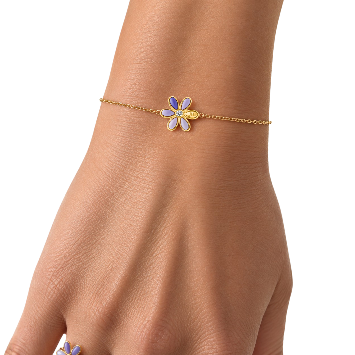 Woman wearing a gold chain bracelet with a lavender enamel flower charm.