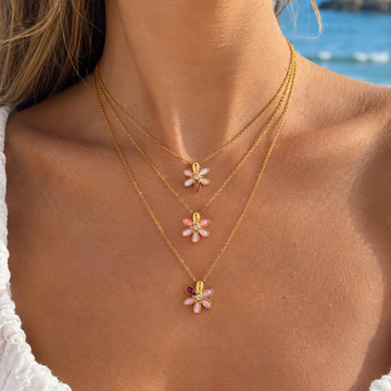 A close-up of a woman's wearing three layered gold chain necklaces with daisy pendants 