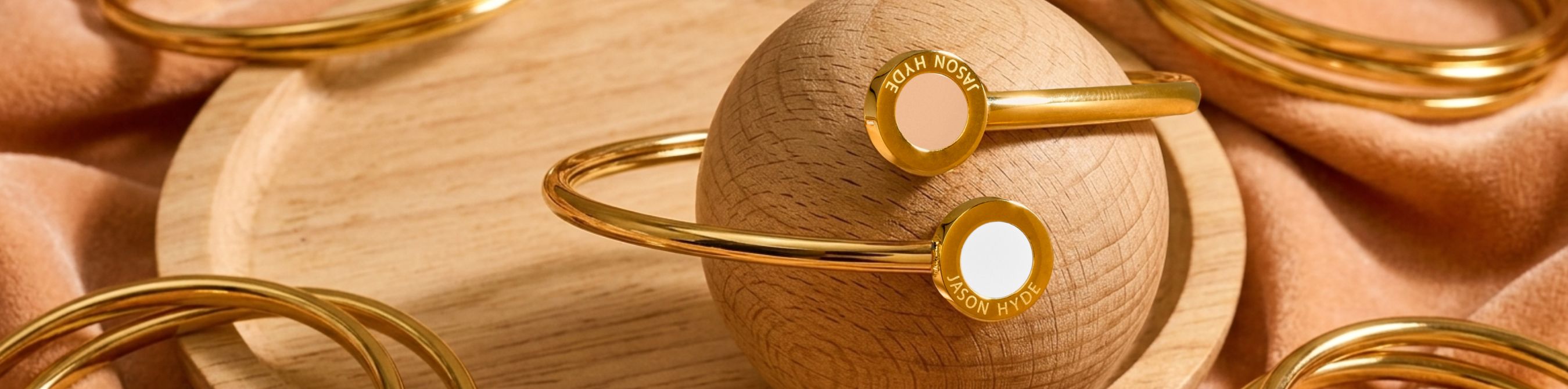 Jason Hyde gold bangle bracelets with white and nude recycled plastic details on a wooden sphere.