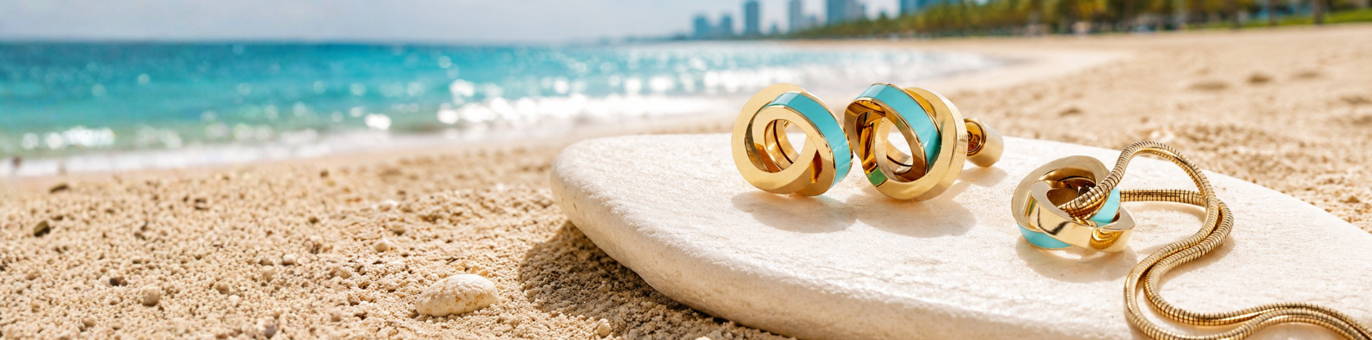 Jason Hyde gold twist earrings and matching necklace with turquoise enamel on a white stone at the beach.