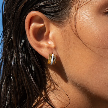 Close-up of a woman wearing Jason Hyde gold huggie hoop earrings with a white center stripe.