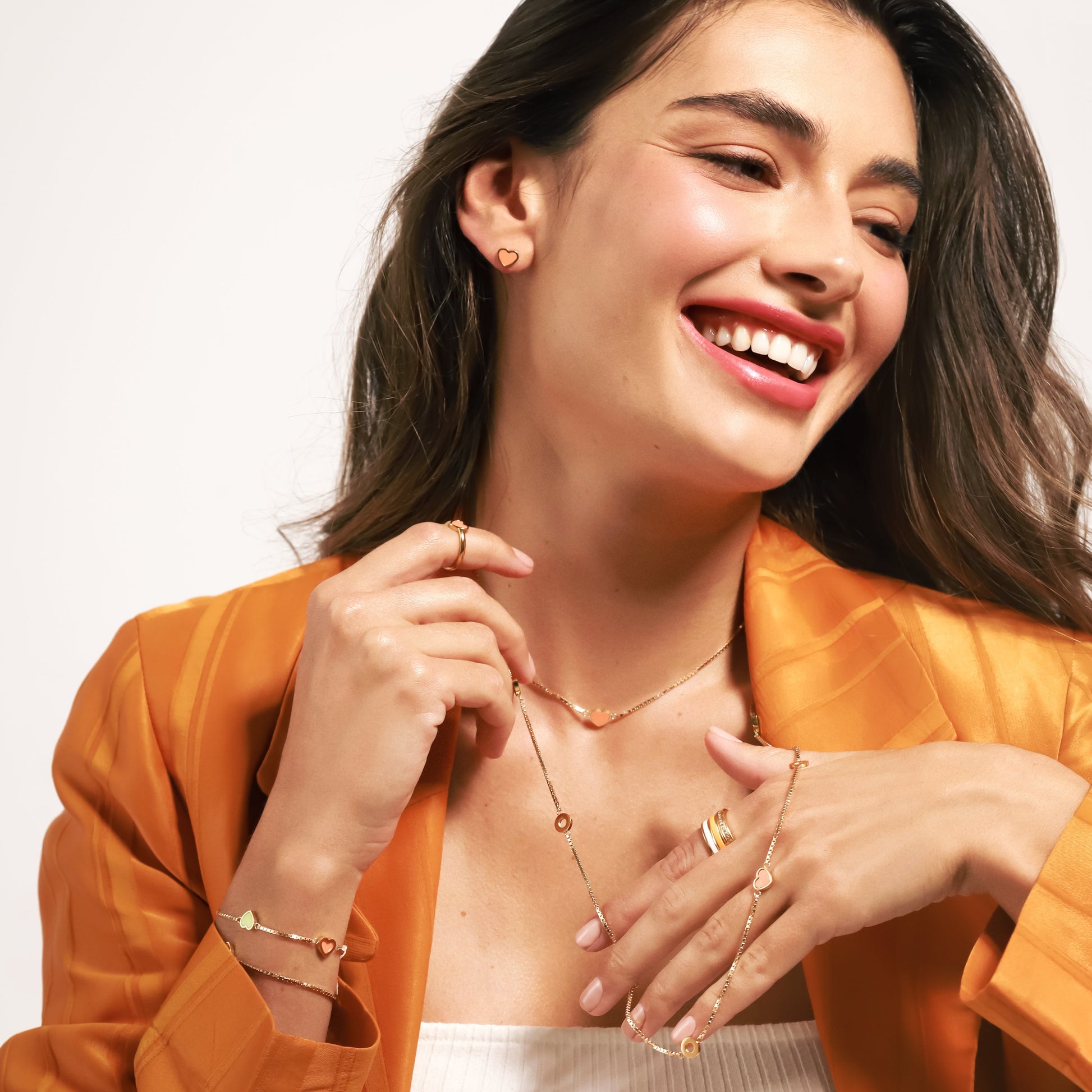 Joyful woman showcasing gold jewelry: heart earrings, necklaces, bracelets, and rings.