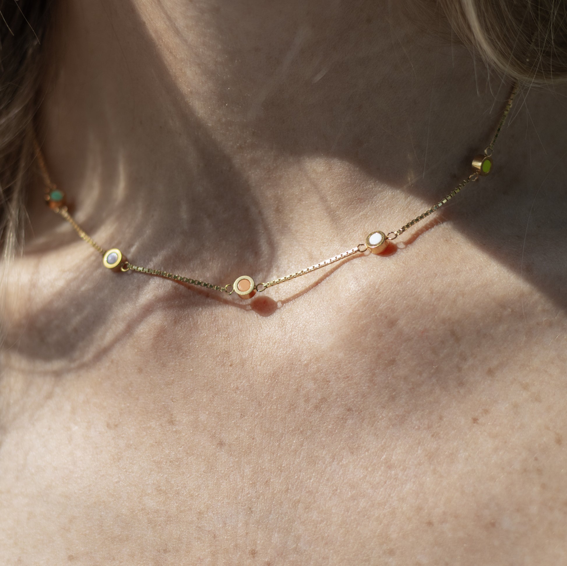 Gold colored necklace with multicolor enamel charms, resting on natural skin tone.