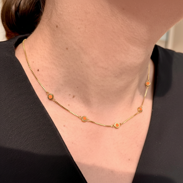 Women's yellow gold-plated necklace adorned with multiple small, spaced-out orange enamel disc pendants.