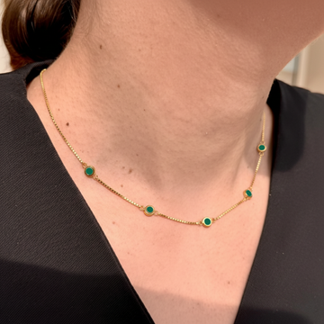 Gold-tone station necklace with small circular green enamel pendants worn over a black top.