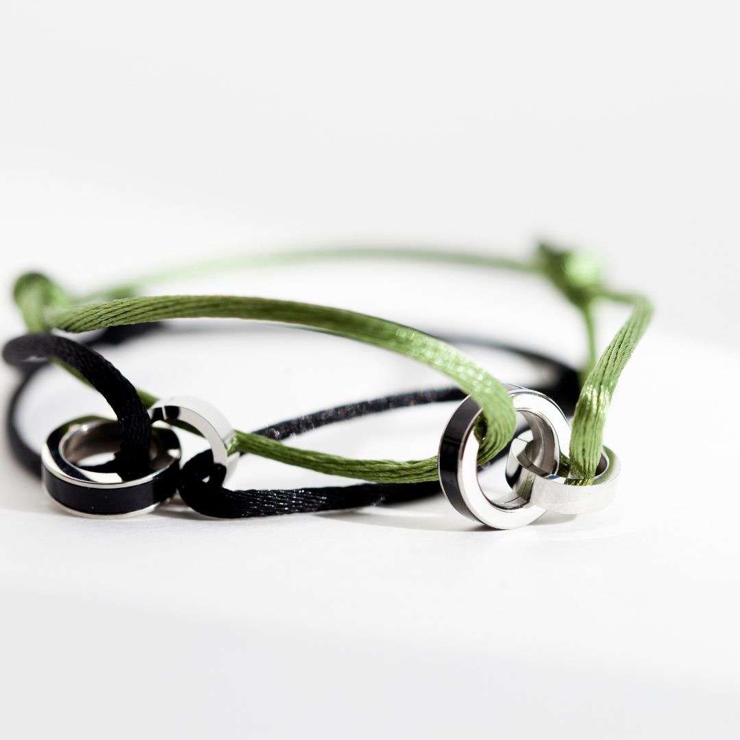Close-up of olive green and black cord bracelets with interlocking silver charms on a white surface.