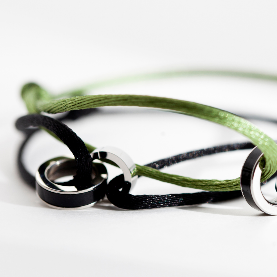 Close-up of olive green and black cord bracelets with interlocking silver charms on a white surface.