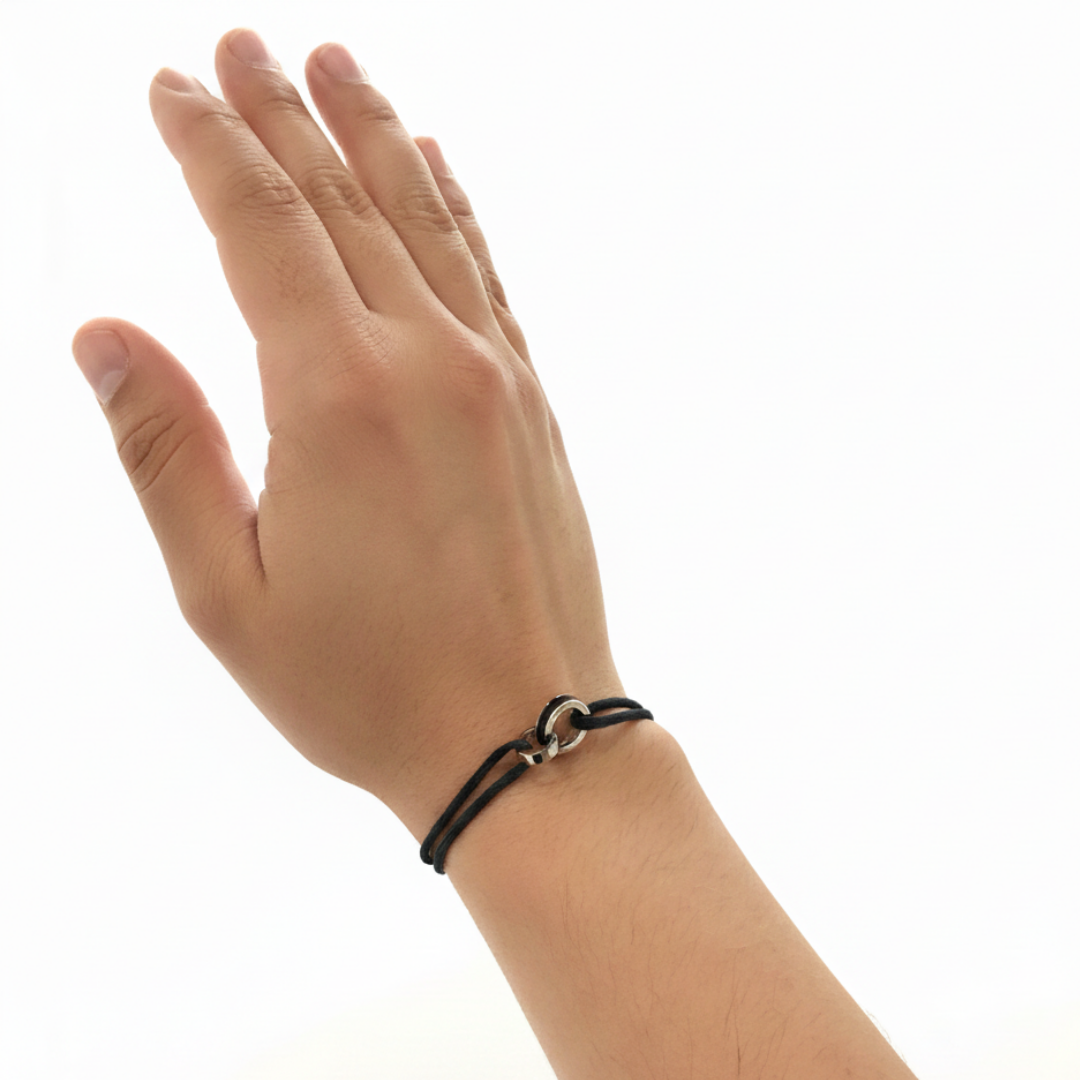 Man wearing a minimalist black cord bracelet with an interlocking silver and black circle charm on a white background