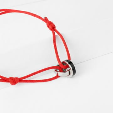 Close-up of a vibrant red cord bracelet with interlocking silver and black rings on a white surface.