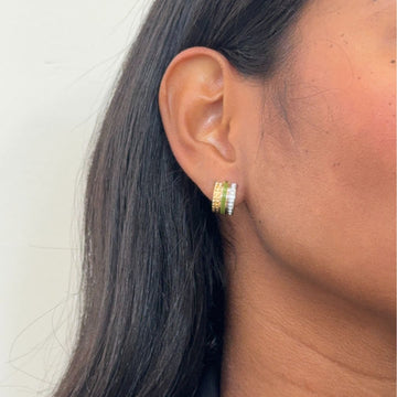 Dainty gold and green enamel huggie hoops worn on a model's ear.