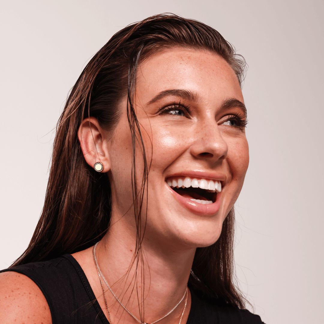 Smiling female model wearing gold stud earrings with cappuccino enamel