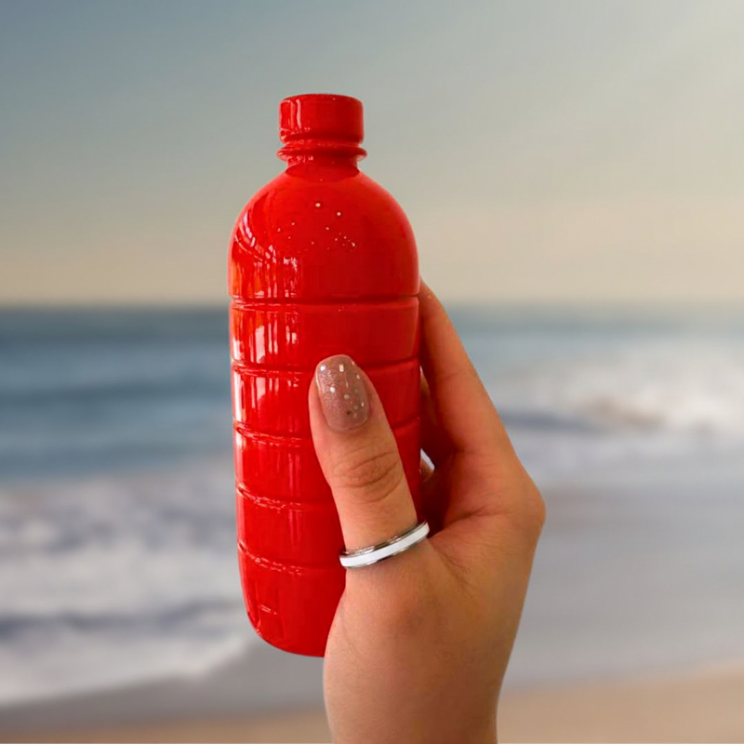 Women's silver and white enamel band ring held against a red bottle with an ocean backdrop.
