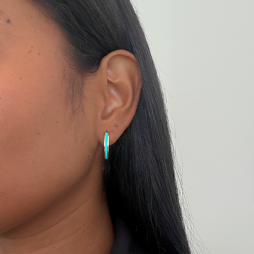 Women's turquoise and silver enamel hoop earrings worn by a model.