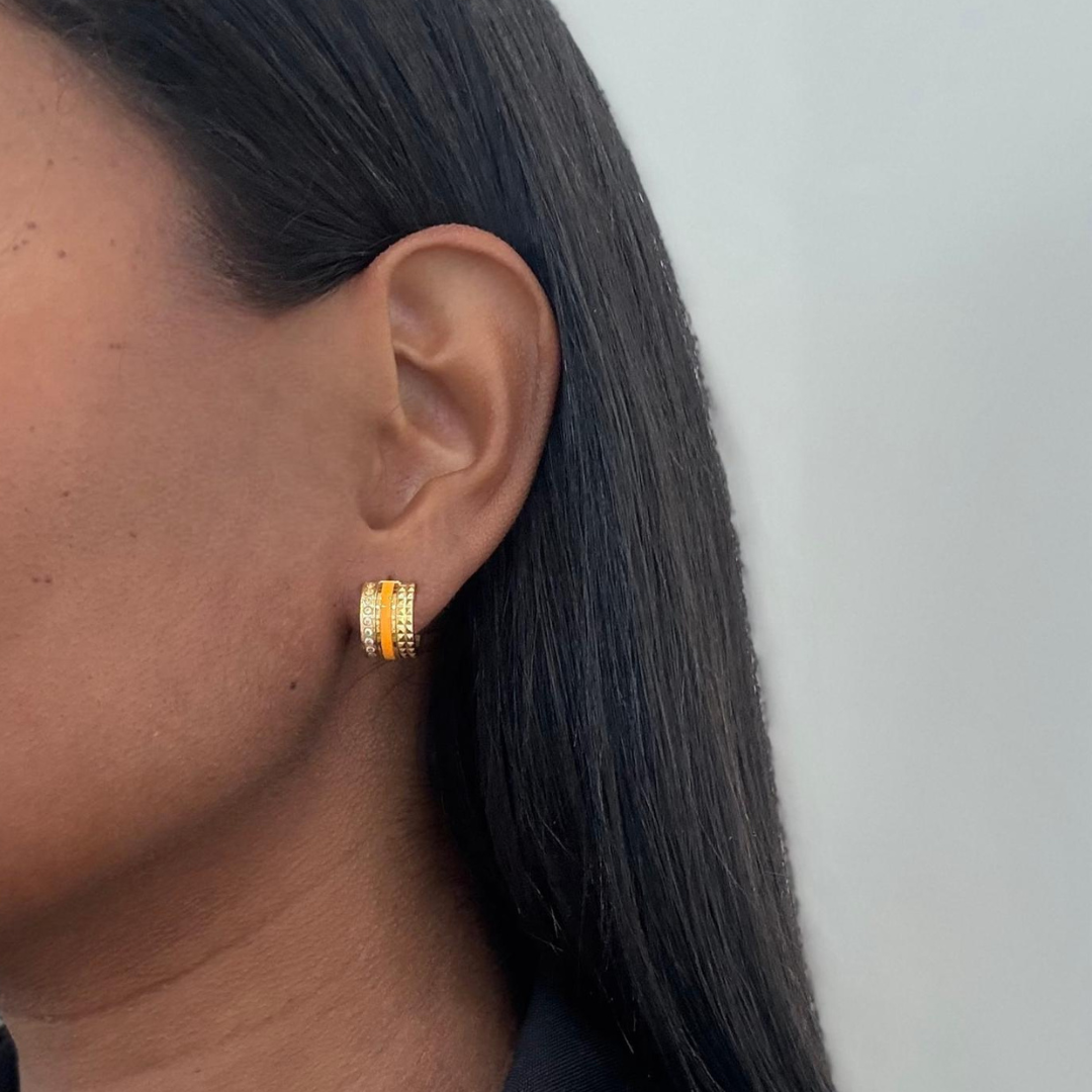 Gold-plated huggie hoop earrings with vibrant orange enamel and crystal detailing on a model.