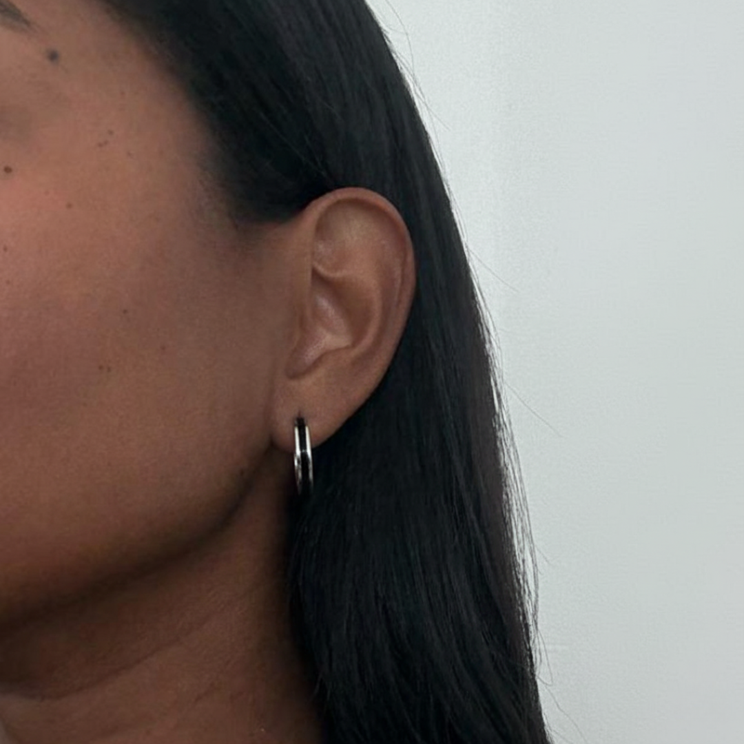 Silver-tone hoop earrings with a thin black enamel inlay worn by a model.