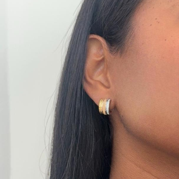 A woman wearing a huggie hoop earring featuring gold, beige enamel