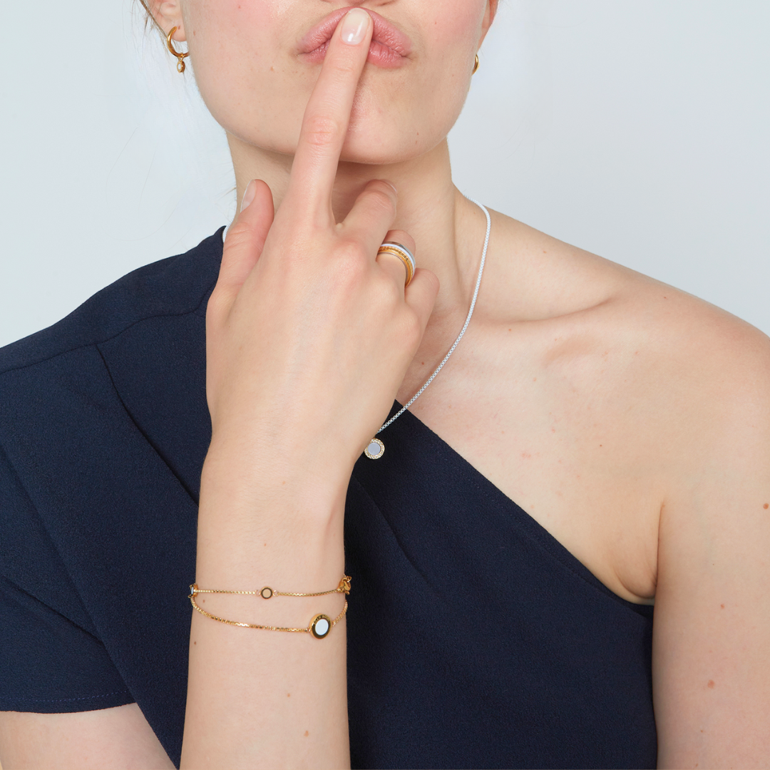 Gold bracelets with round enamel charms and minimalist details, styled on woman