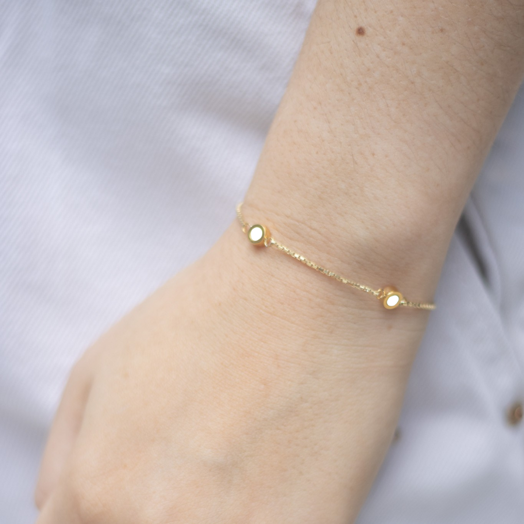 Minimalist gold bracelet by Jason Hyde featuring white enamel circle charms