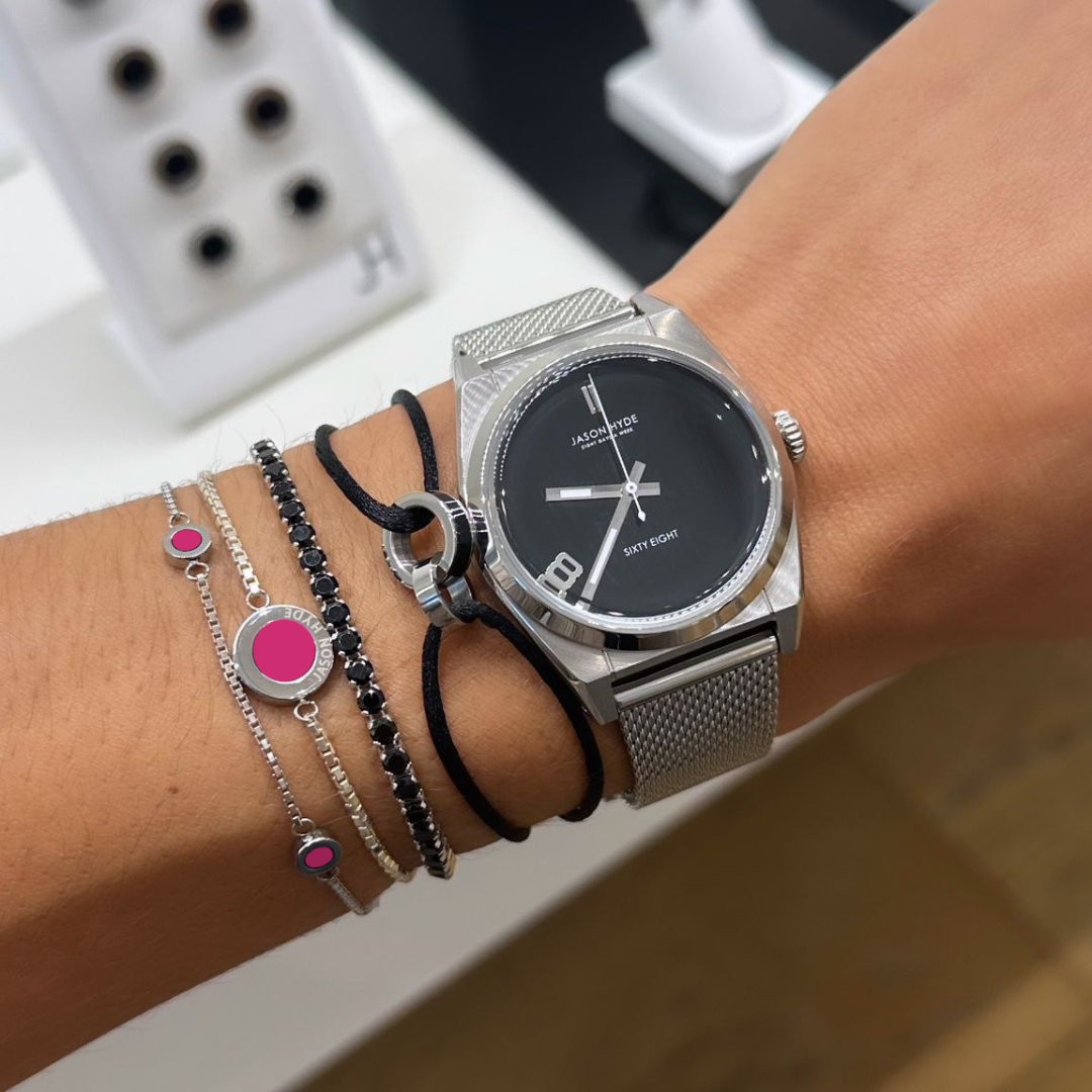 Silver jason hyde watch and several silver and black bracelets on one wrist.