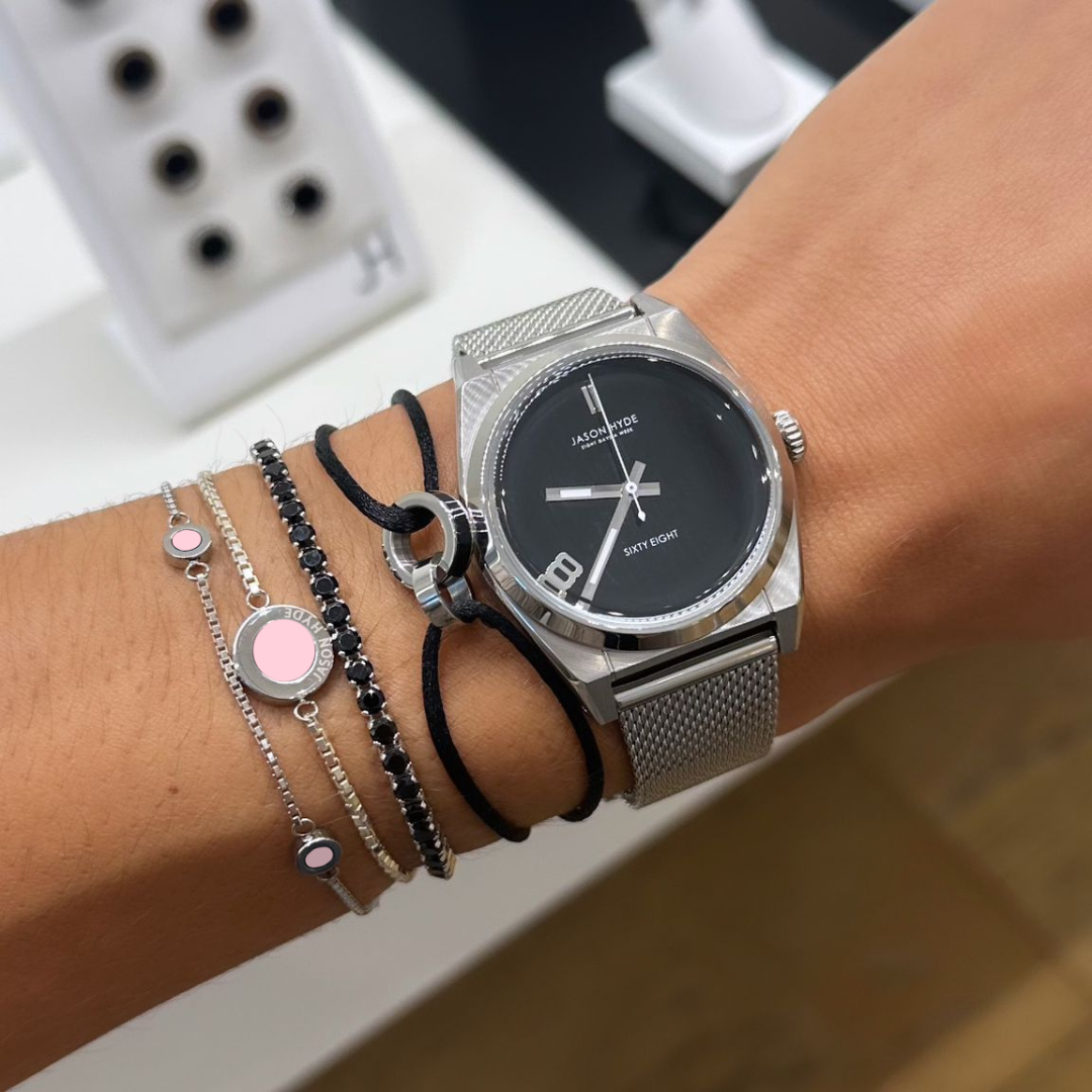 Wrist with silver jason hyde watch and multiple silver chain and black cord bracelets.