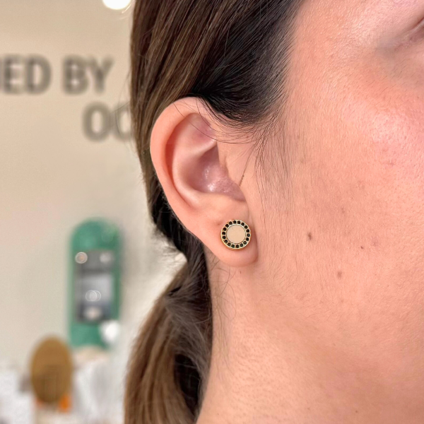 Jason Hyde gold circle stud earring with black enamel accents, worn on woman’s ear