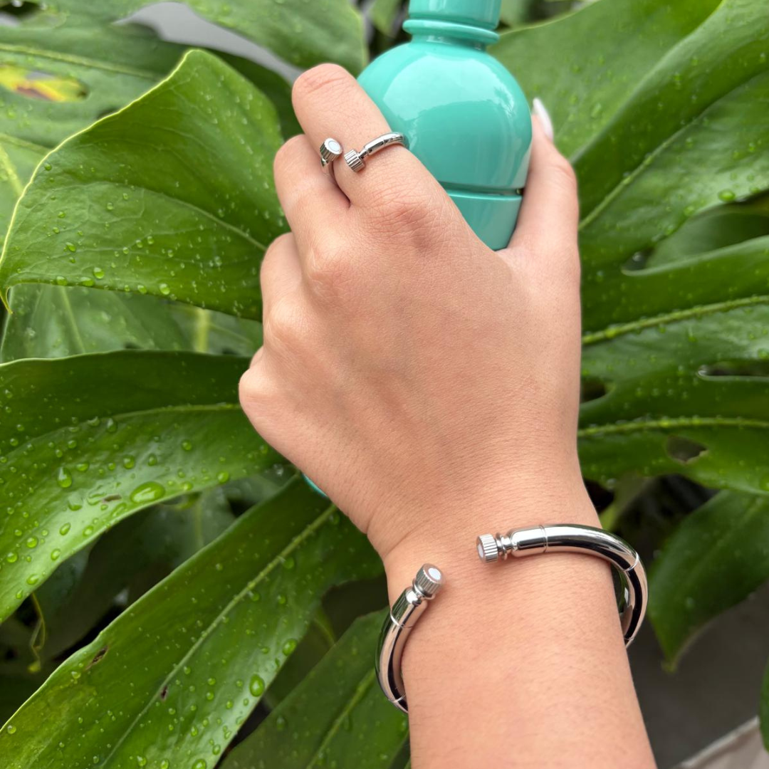 Hand holding a teal bottle, wearing a silver ring and a silver Seacap bangle