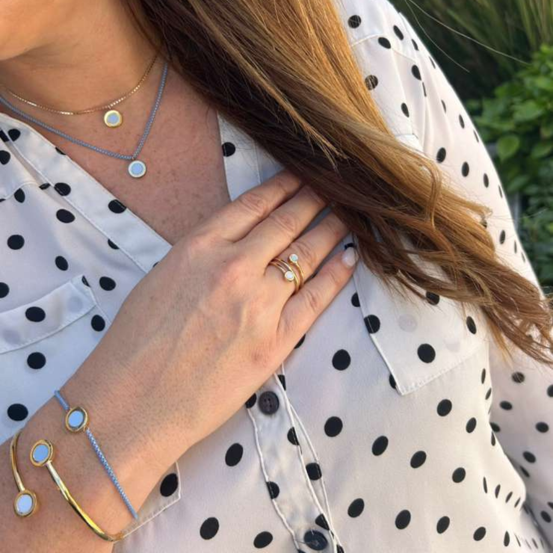 Woman in polka-dot shirt wearing gold necklaces, a ring, and a bracelet, all with powder blue charms