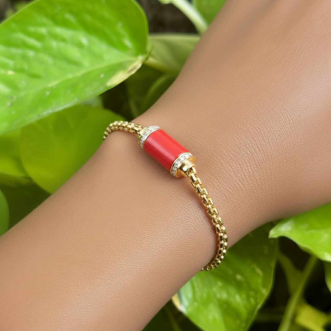 Gold chain bracelet with red cylinder and zirconia details on a wrist