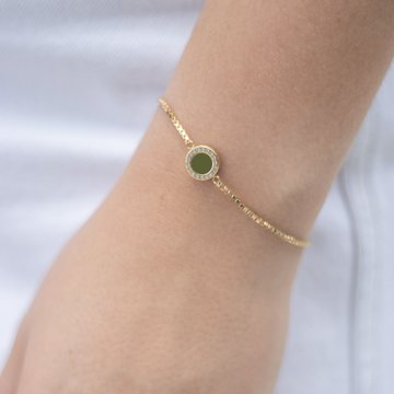 Close-up of a delicate gold bracelet featuring a round pendant with a ring of small zirconias