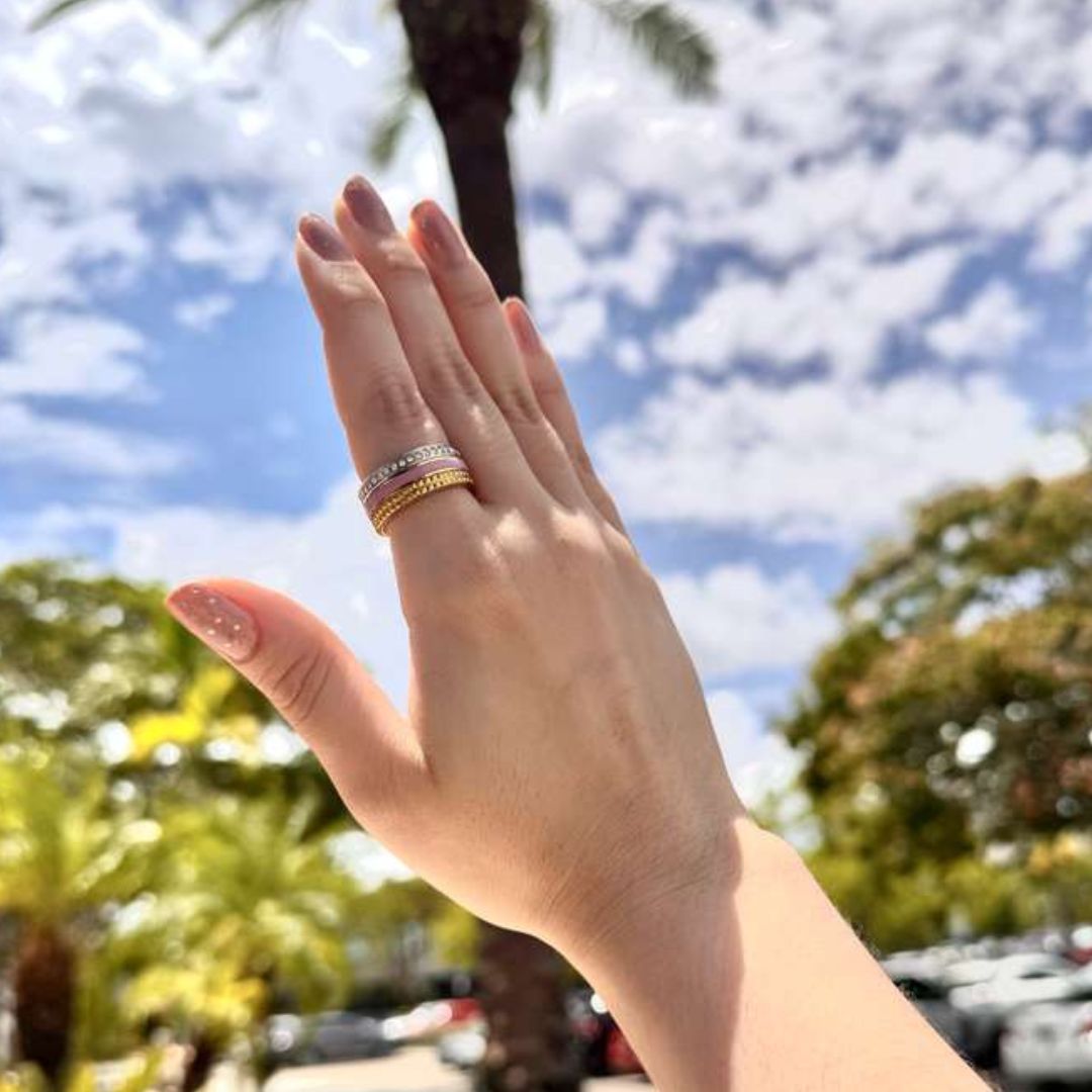 A hand with a Wewa Tube Beige Chip Ring, against a backdrop of a blue sky.