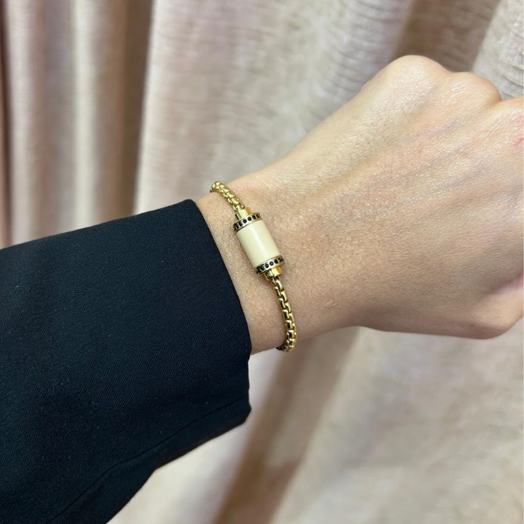 Gold bracelet with white cylinder and black accents on a wrist.