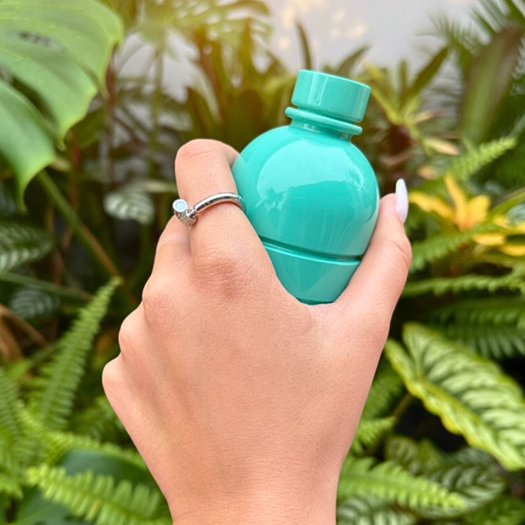 Hand holding a small teal bottle, with a silver ring on the index finger.