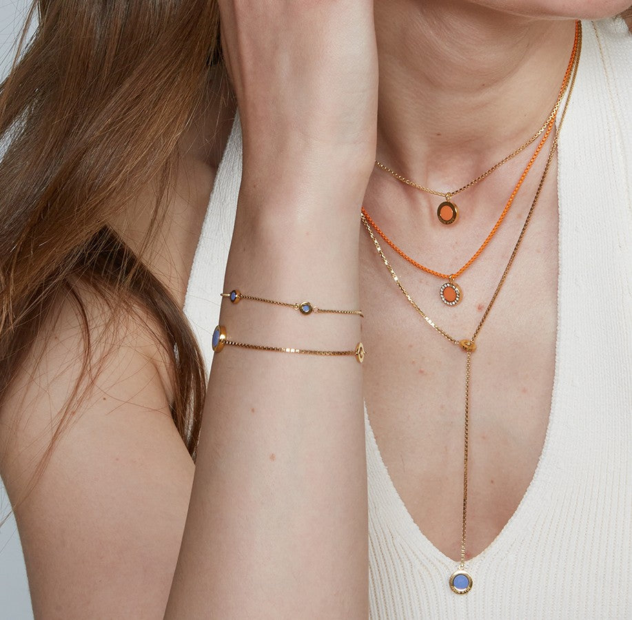 Gold necklaces and matching bracelets with vibrant ocean plastic details styled on chest and wrist.