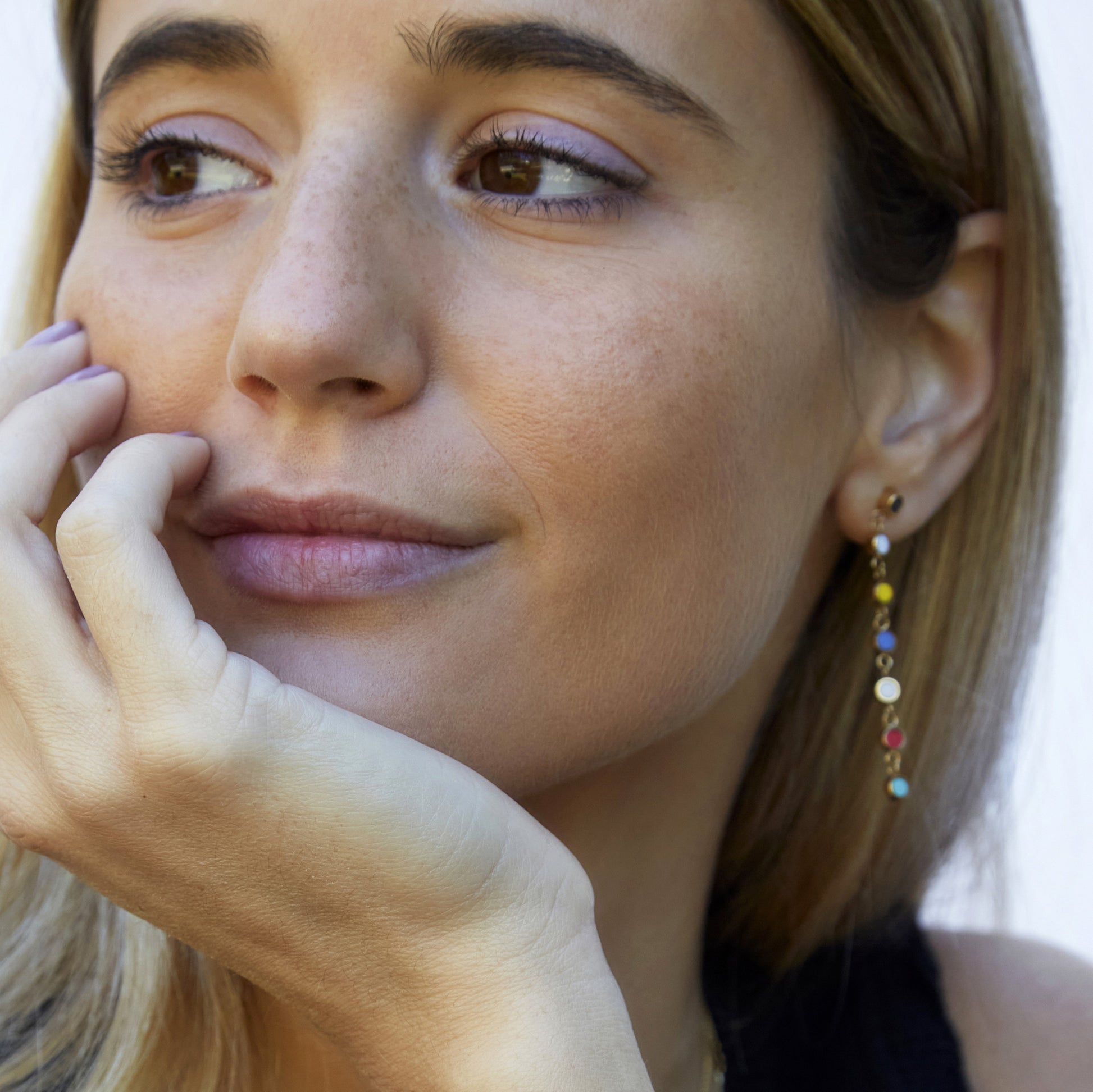 Smiling woman wearing long gold drop earring with colorful recycled ocean plastic charm